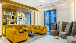 Una sala de estar moderna con un conjunto de sofá amarillo, un sofá gris y una mesa de centro. Se observa una estantería con objetos decorativos y un ventanal con vistas al exterior.