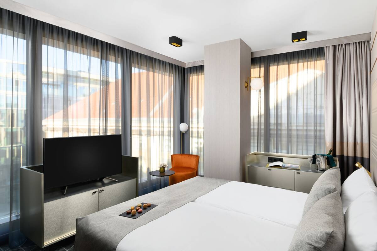 A modern hotel room with a large bed, a flat-screen TV, a small table with a vase, and a chair.