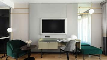 A modern hotel room with a desk, two chairs, a TV, and a small table with a vase.