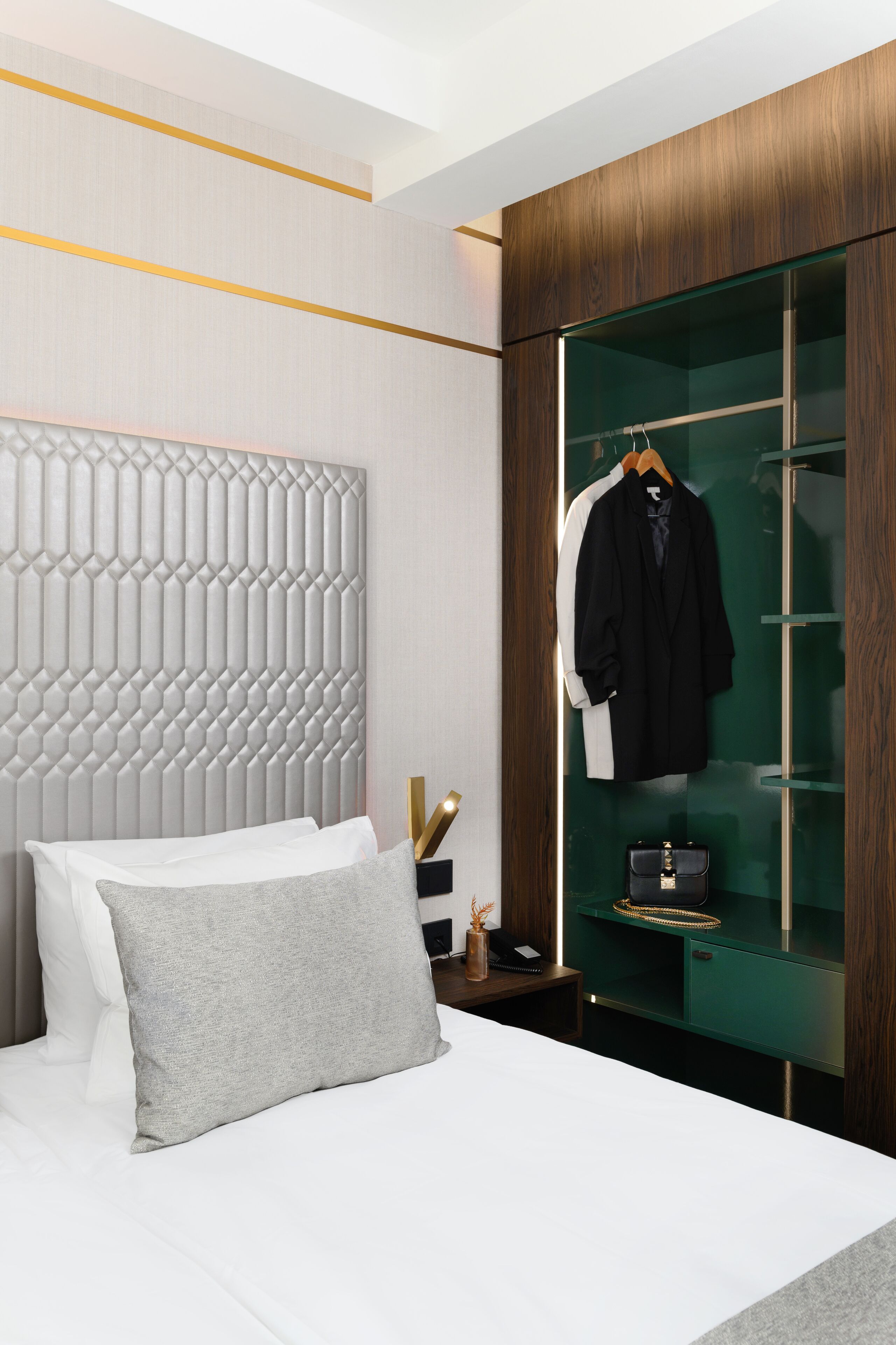 A modern hotel room with a bed, a wardrobe with a mirror, and a coat hanging inside.