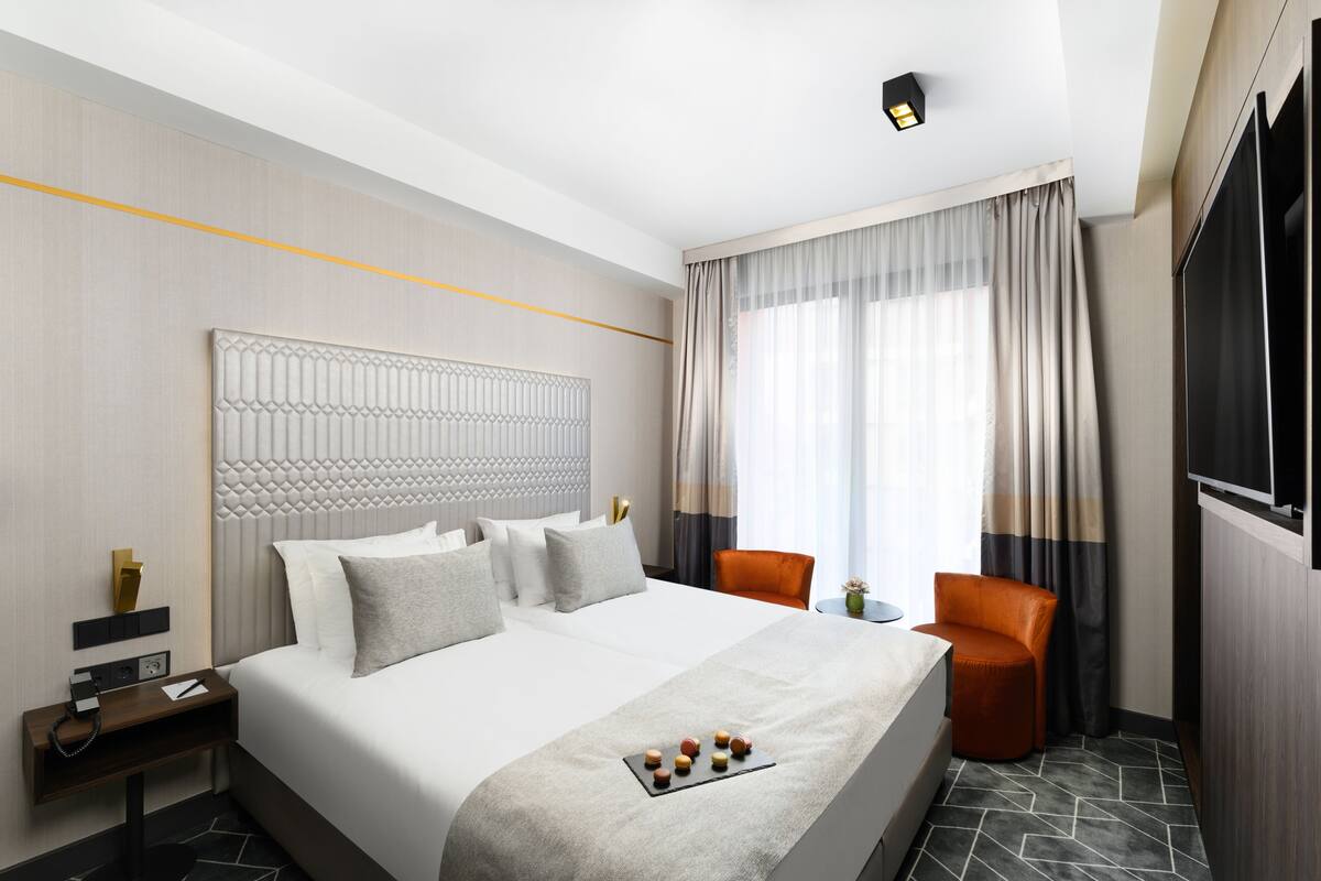 A hotel room with a large bed, a bedside table with a lamp, a small table with a vase, and a chair.