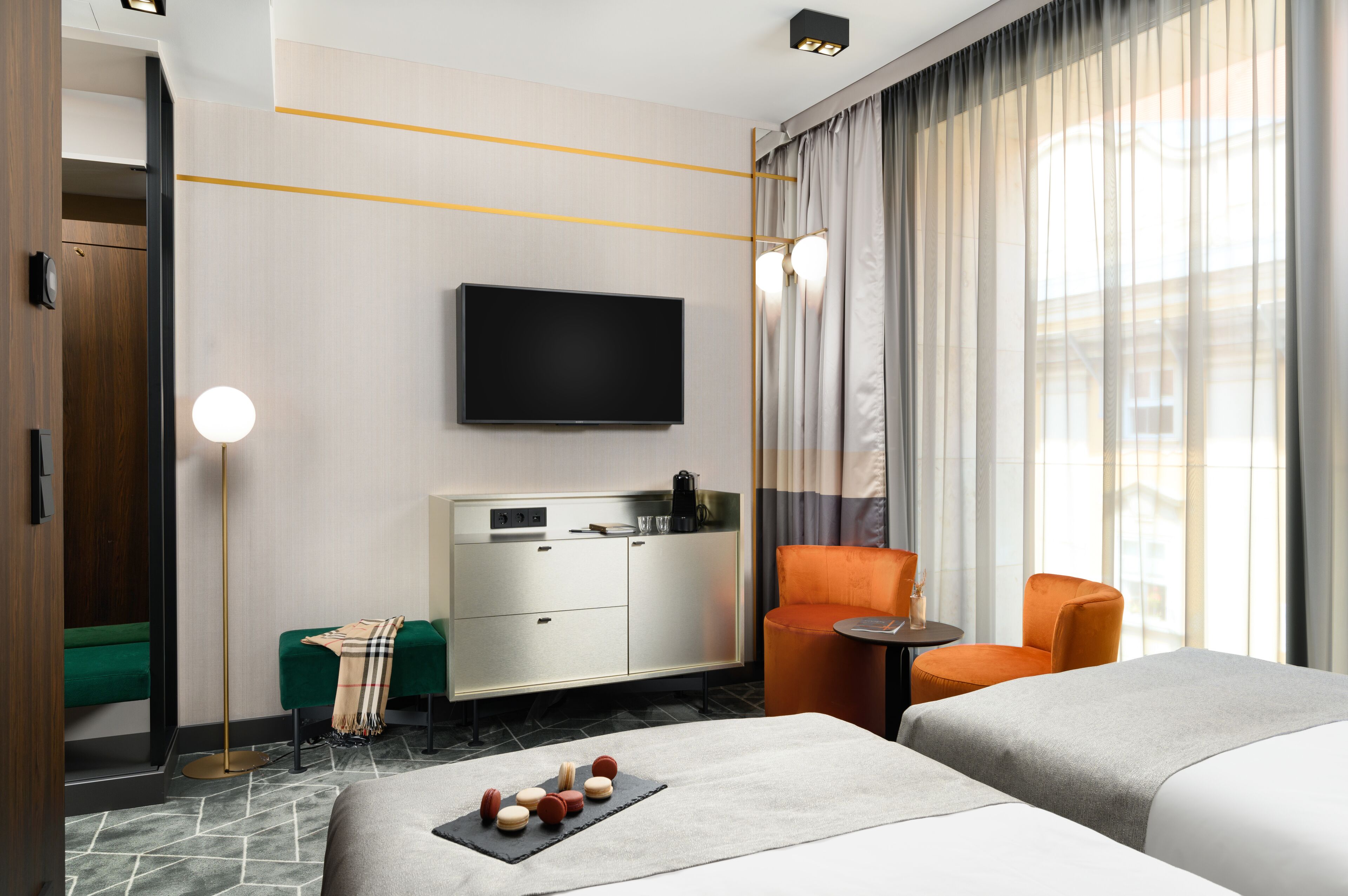 Una camera d'albergo con un letto, una scrivania, una sedia, una televisione e una finestra con tende.