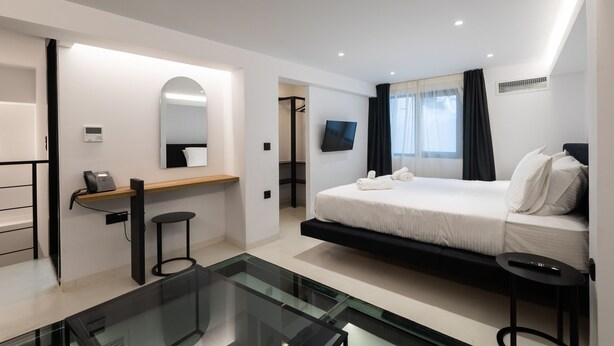 Une chambre d’hôtel moderne équipée d’un lit, d’un bureau, d’un miroir, d’une télévision et d’une table en verre.