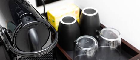 A coffee machine, a box of coffee pods, and two black cups on a tray.