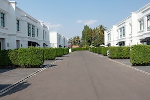 Eine Straße gesäumt von weißen Gebäuden, ein klarer Himmel und ordentlich gestutzte Hecken.
