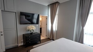 Quarto de hotel com uma cama grande, uma televisão de tela plana na parede, um aparador de madeira escura e um vaso com flores brancas.