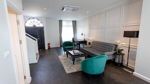Uma sala de estar moderna com piso de madeira escura, uma poltrona verde, um sofá e uma mesa de centro.