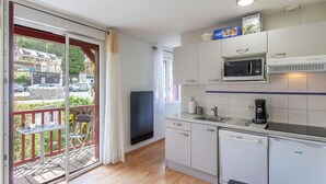 A compact kitchen with a microwave, coffee maker, and dishwasher. A large window offers a view of the street. - Apartment Near Cable Car, Shops & Amenities, East-Facing with Balcony (Cauterets)