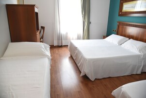 Habitación de hotel con dos camas individuales, cabeceros de madera, un armario de madera y un amplio ventanal con cortinas.
