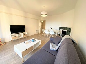 A modern living room with a flat-screen TV, a sofa, a coffee table, and a dining area with chairs and a table.