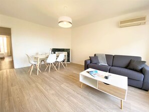 Una sala de estar moderna con un sofá gris, una mesa de centro blanca y un comedor con mesa y sillas.