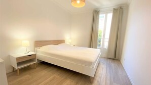 A bedroom with a bed, bedside tables, and a window with curtains. - Ajaccio: Appartement 3 pièces, 6 couchages, 600m de la plage, climatisé, centre-ville (Ajaccio)
