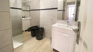 A modern bathroom with a white sink, mirror, and tiled walls. There are two black baskets on the floor. - Ajaccio: Appartement 3 pièces, 6 couchages, 600m de la plage, climatisé, centre-ville (Ajaccio)