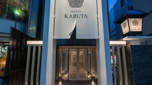 La entrada del Hotel Karuta, con un diseño moderno, presenta un logotipo y el nombre del hotel bien visibles sobre la entrada.
