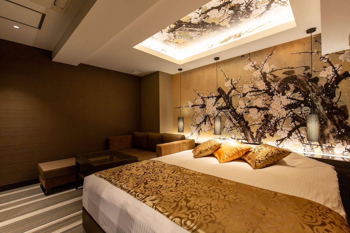 Quarto de hotel com uma cama grande, um sofá, uma mesa pequena e uma obra de arte na parede.