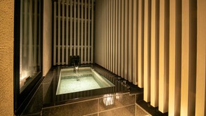 Un baño moderno con una bañera rectangular, un cerramiento de vidrio y un diseño de pared a rayas verticales.