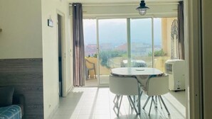 A room with a dining table and chairs, a ceiling light, and a view through a glass door to an outdoor area with a chair and a table. - Cozy 1BR Apartment with Parking, 700m from Calvi Beach (Calvi)