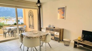 A dining area with a round table and chairs, a cabinet with drawers, a television, and a framed picture on the wall. - Cozy 1BR Apartment with Parking, 700m from Calvi Beach (Calvi)