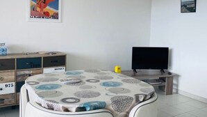 A room with a round table, a television, a cabinet, and a poster on the wall. - Cozy 1BR Apartment with Parking, 700m from Calvi Beach (Calvi)