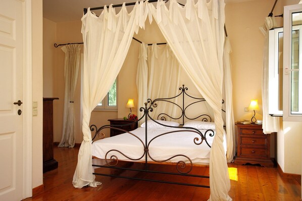 Un dormitorio con cama con dosel, mesita de noche, lámpara y ventana con cortinas.
