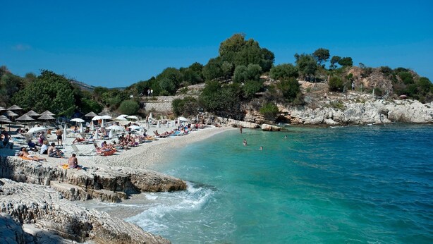 A beach with clear turquoise water, rocky shore, and umbrellas. - Villa Berry (Corfu)
