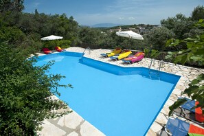 Piscina com deck de pedra, rodeada por vegetação exuberante e vista para uma cidade ao longe.