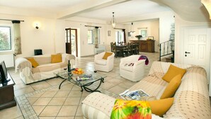 A spacious living room with a sofa set, a coffee table, and a dining area in the background. - Villa Berry (Corfu)