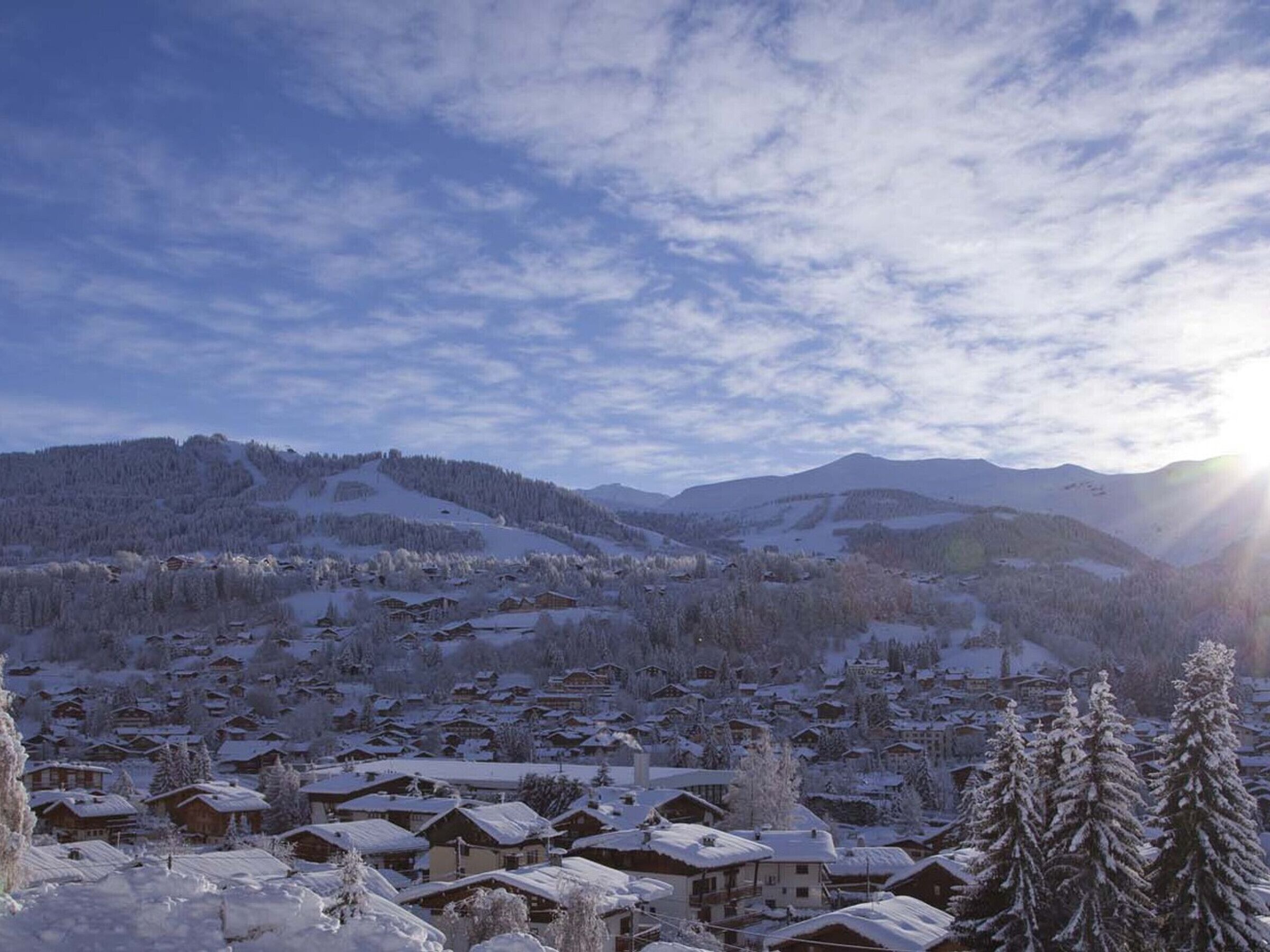 A snow-covered village with traditional wooden houses, a mountain backdrop, and a clear sky.