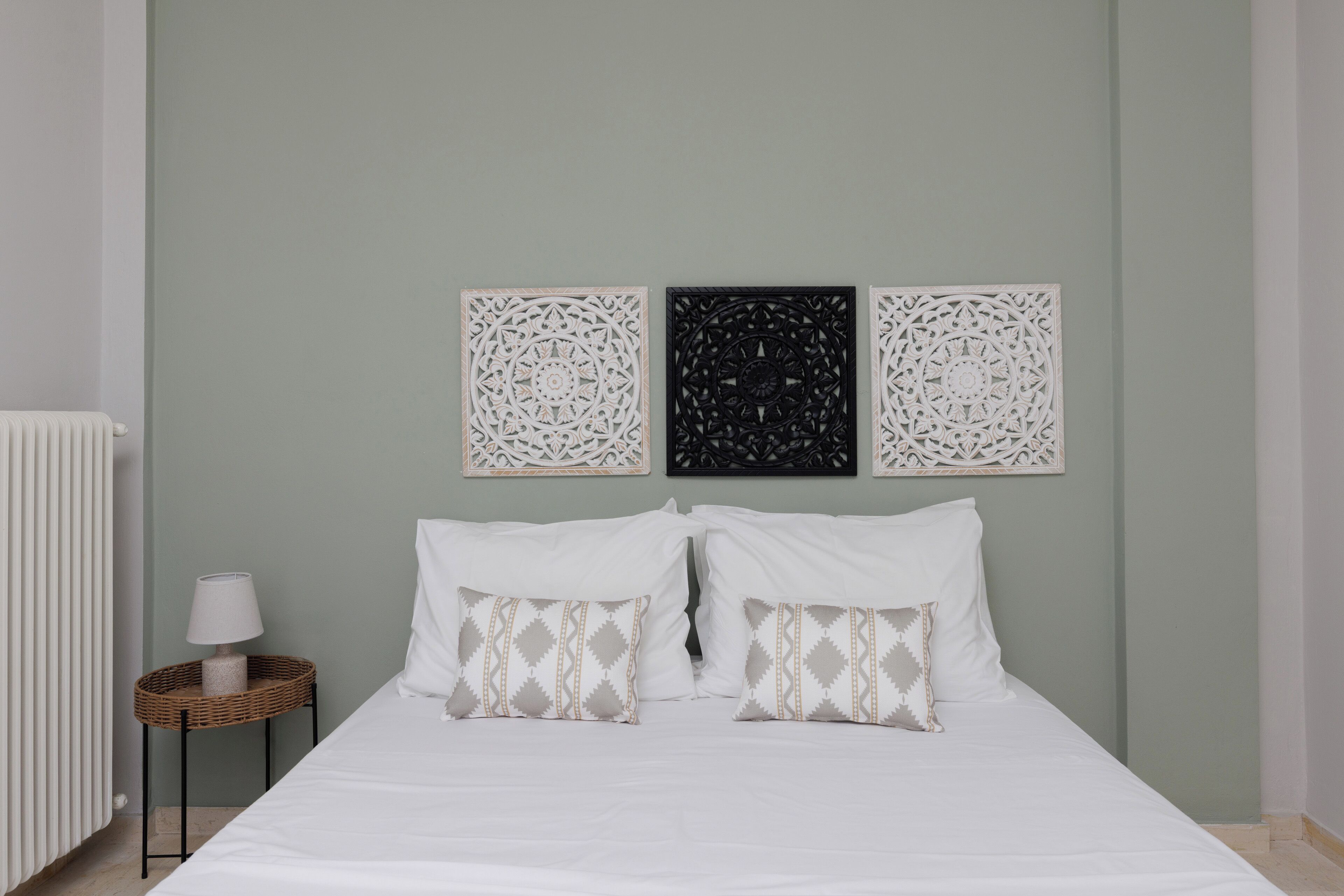 A neatly made bed with patterned pillows, a small side table with a lamp, and three wall art pieces above the bed.