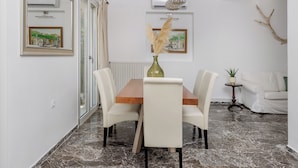 Un comedor con una mesa de madera y sillas blancas, un jarrón con pastos secos y un aire acondicionado instalado en la pared.