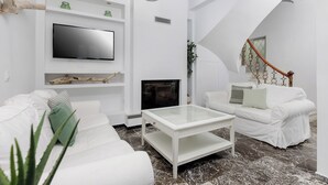Una sala de estar moderna con un sofá blanco, una mesa de centro de vidrio, un televisor de pantalla plana y una chimenea.