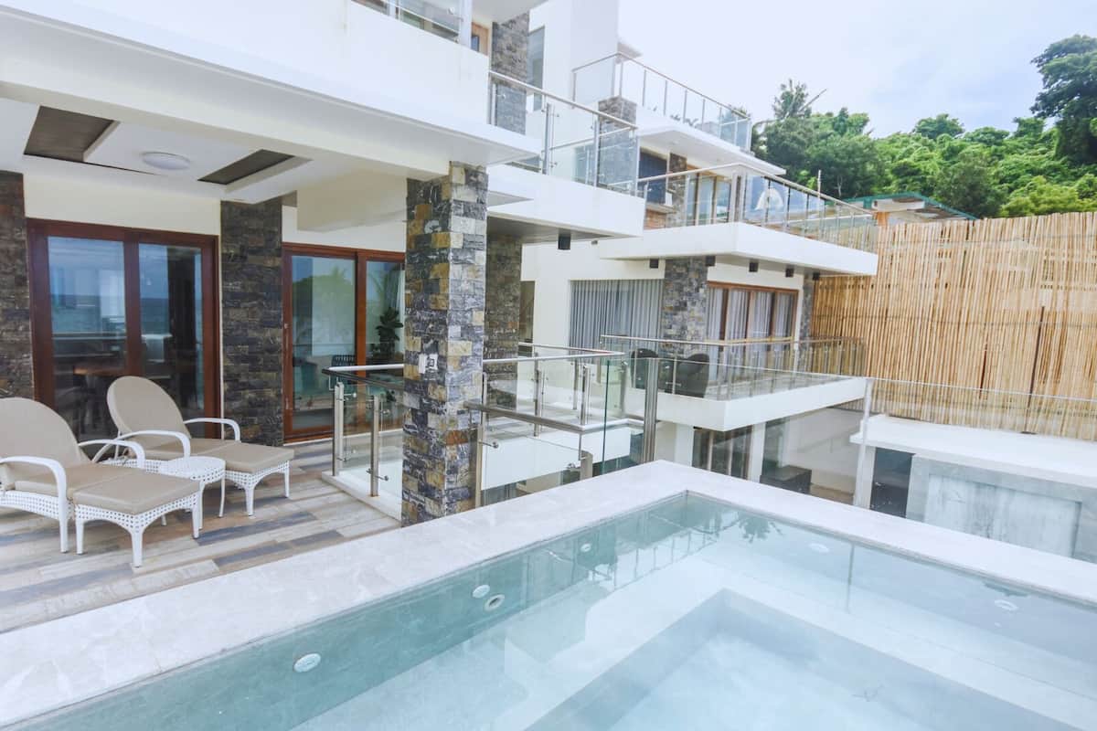 A modern house with a swimming pool, stone pillars, and a balcony with glass railings.