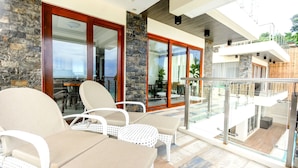 A balcony with white wicker furniture, a stone wall, and a glass door leading to an indoor area with a view of the sea.