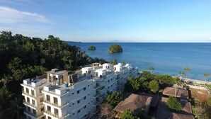A modern hotel with multiple floors, a rooftop terrace, and a view of the sea and islands.