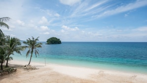 A beach with clear turquoise water, a sandy shore, and a small island in the distance.