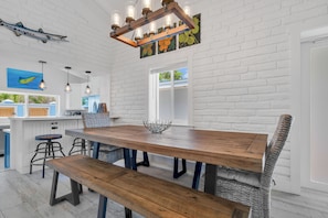 A modern kitchen with white brick walls, a wooden dining table, bar stools, and pendant lighting.