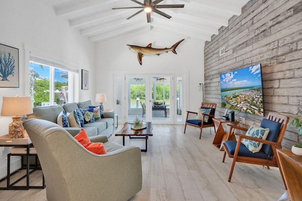 A spacious living room with a ceiling fan, a mounted shark, and a large TV on a brick wall.