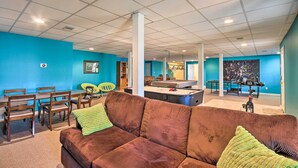 Une pièce spacieuse avec une table de billard, un canapé marron agrémenté de coussins verts et un mur bleu.