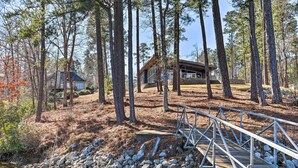 Une cabane entourée de grands pins, un pont de bois et une rive rocheuse.