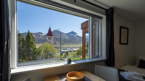 Habitación de hotel con un ventanal que ofrece vistas a una iglesia y montañas.