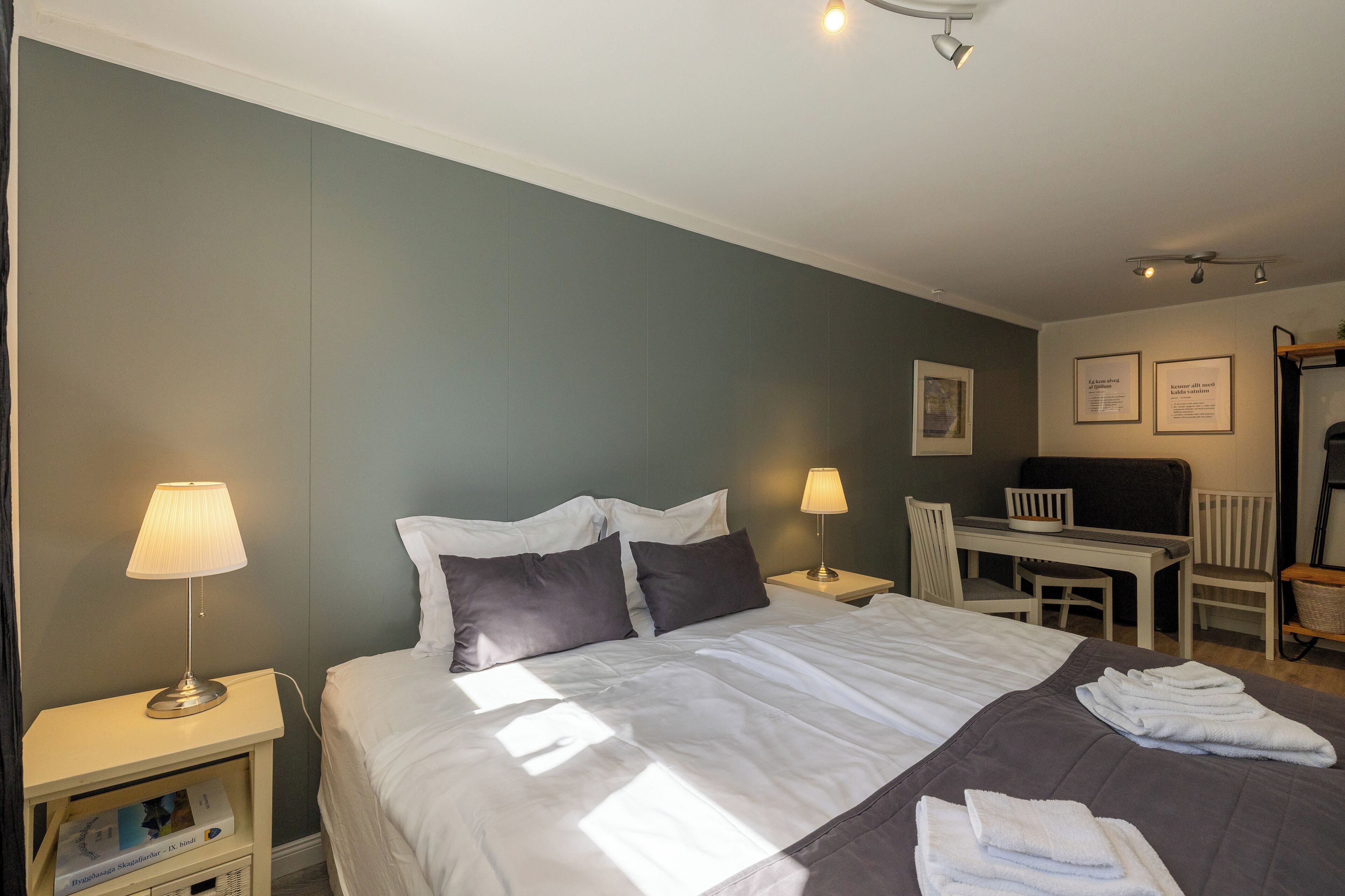 A hotel room with a large bed, two bedside tables with lamps, a desk with a chair, and a small seating area with a chair and a bench.