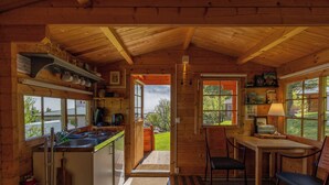 Interior de una cabaña de madera con cocina, comedor y vistas al exterior.
