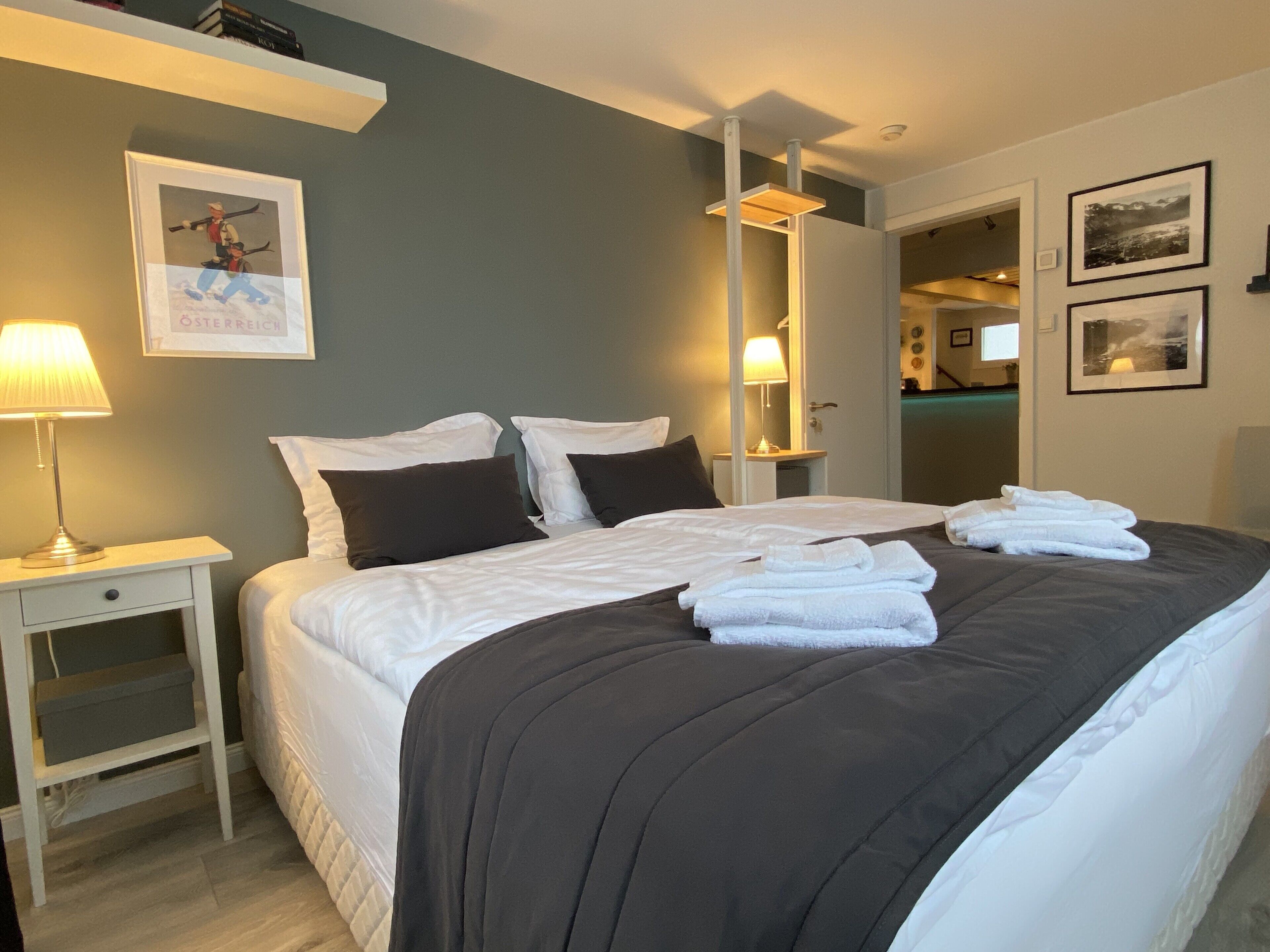 A neatly made bed with white and dark bedding, a bedside table with a lamp, and a framed picture on the wall.
