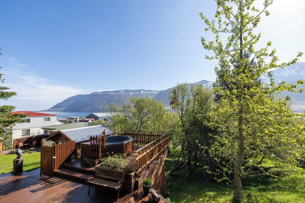 A wooden deck with a hot tub, a small building, and a view of mountains and a lake.