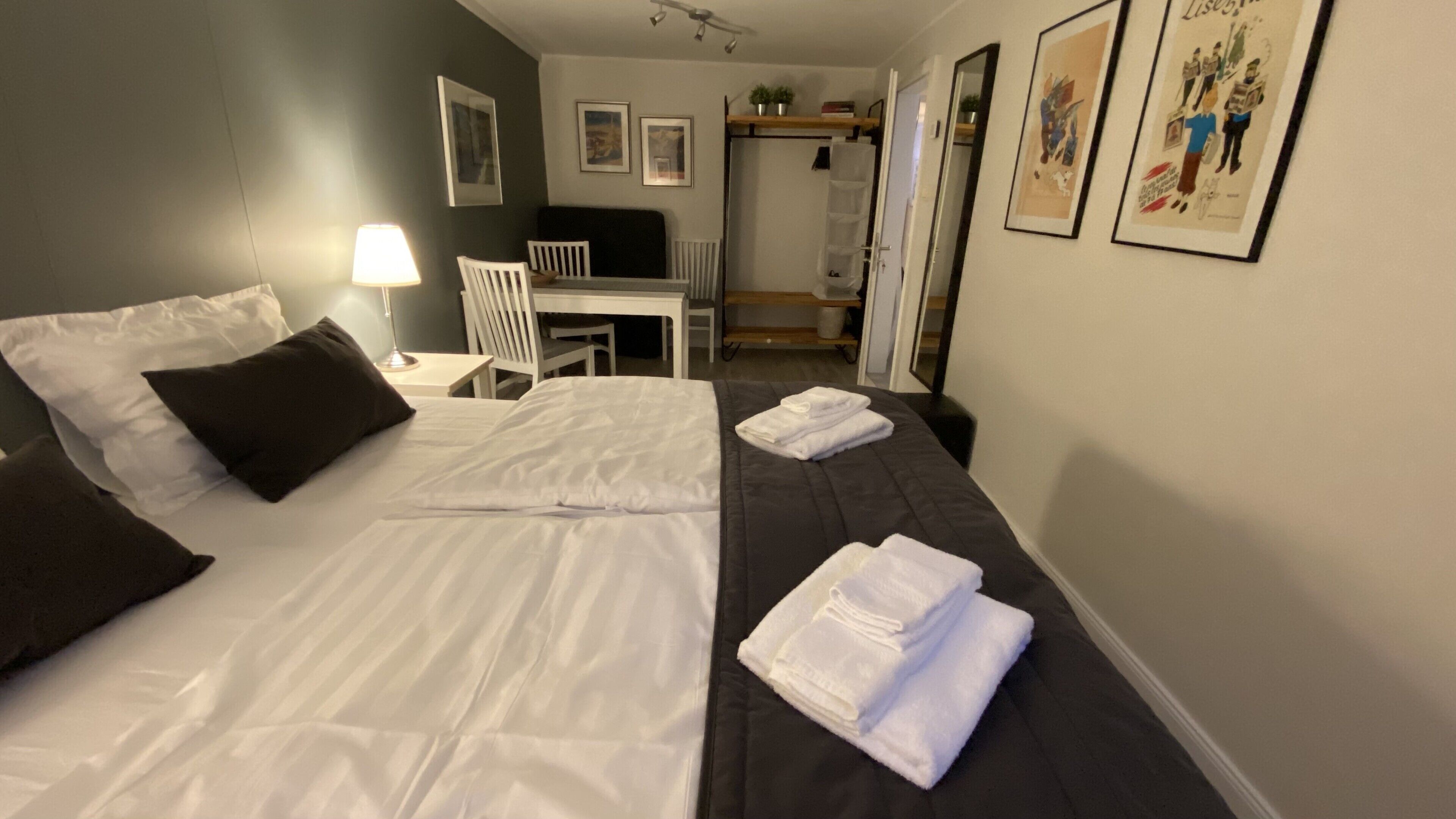 A hotel room with two beds, a desk, a chair, and a small table. There are towels on the beds and a lamp on the desk.