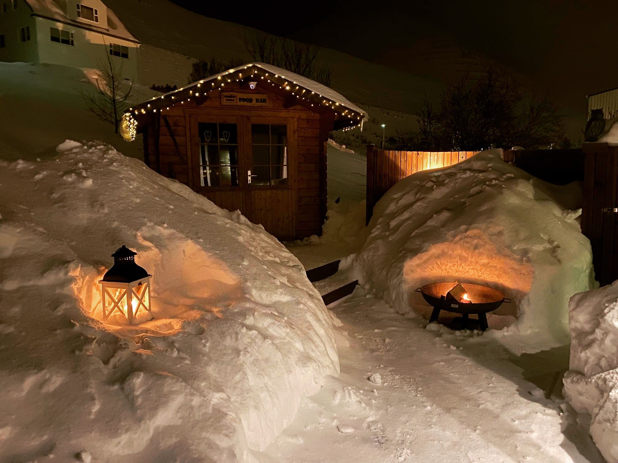A snow-covered outdoor area with igloos and a wooden cabin with lights.