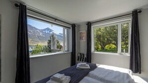 Habitación de hotel con cama, ventana con vista a la montaña y un perchero negro.