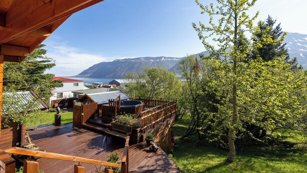 Una terraza de madera con un jacuzzi, una valla de madera y vistas a montañas y un lago.