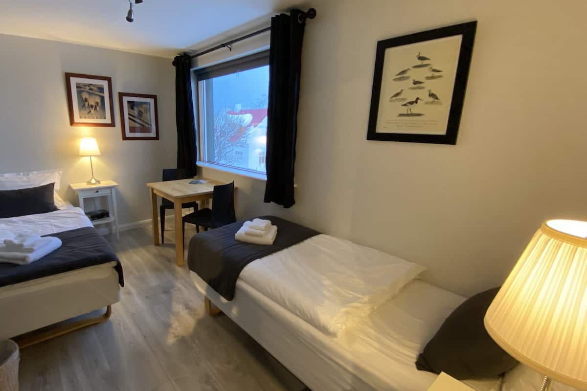 A hotel room with two beds, a desk, a chair, a lamp, and a window with curtains.