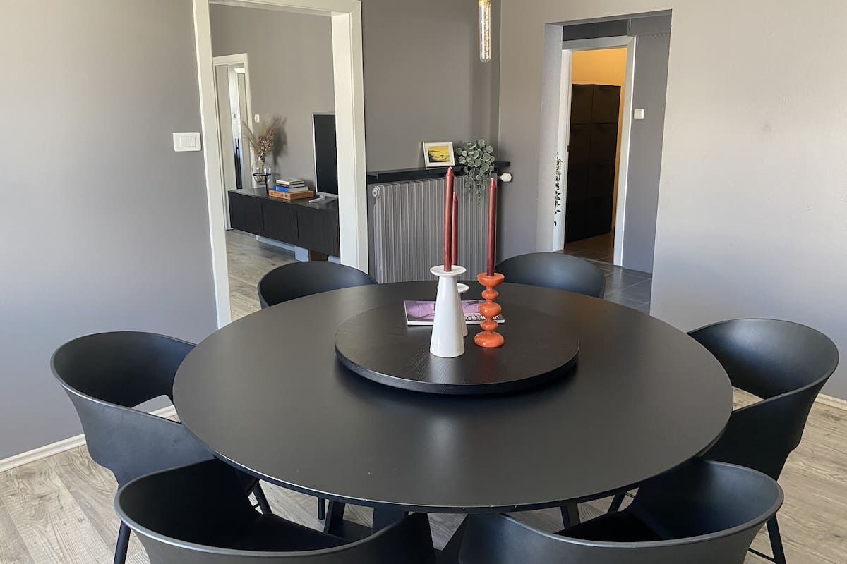 A modern dining area with a round table, black chairs, and a white vase with candles.